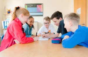 Fünf Kinder lösen an einem Tisch gemeinsam Aufgaben bei Nachhilfe CollegLine